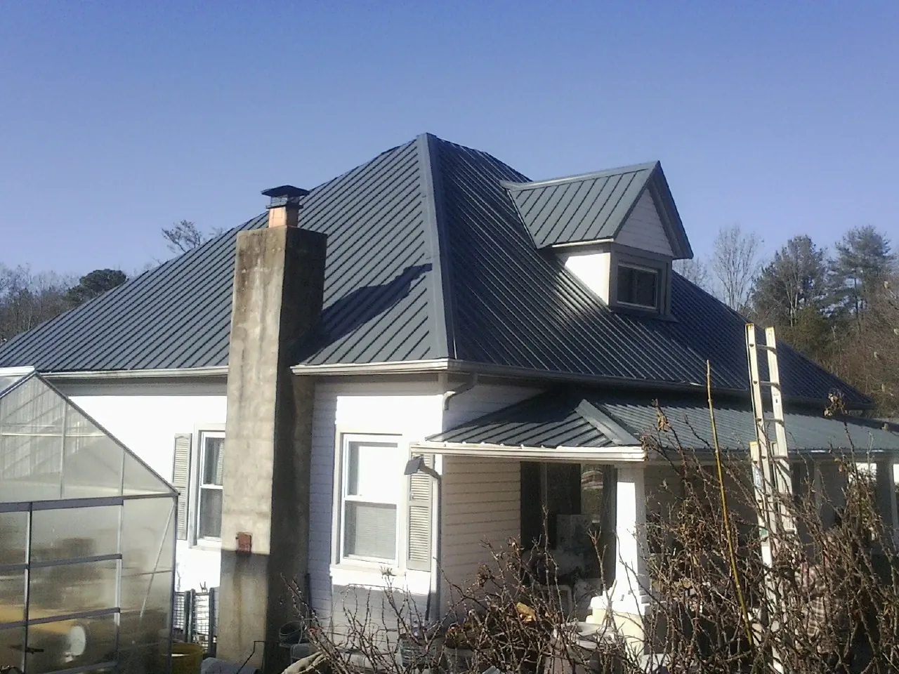 Dark blue standing seam metal roof on a white farmhouse with dormer — Slate & Tile Roof Repair by Roofing Brothers in Lowry City