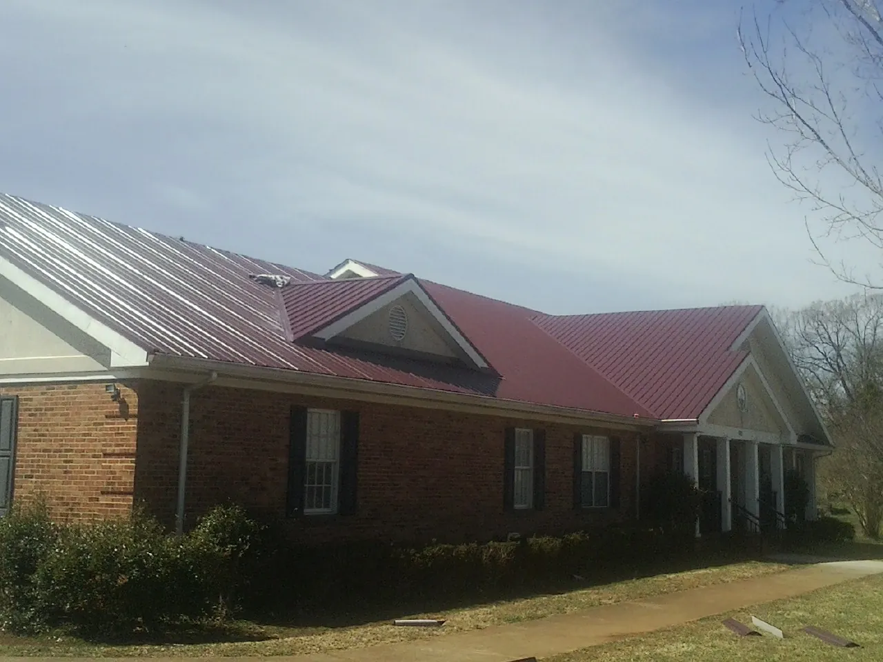 Red metal roof with gabled entries on a long brick building, from a Hail Damage Roof Repair job in Lowry City