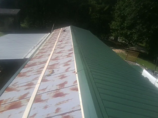 Old rusted panels beside newly installed green metal roofing — Wind Damage Roof Repair by Roofing Brothers in Lowry City