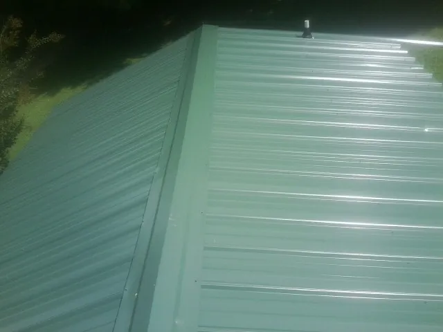 New green metal panels meeting at the ridge of a roof — Flat Roof Repair work by our crew in Lowry City