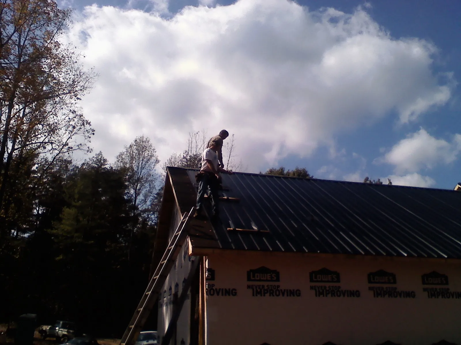 Roofer fastening dark metal panels high against a cloudy sky, from a Roof Inspection job in Lowry City