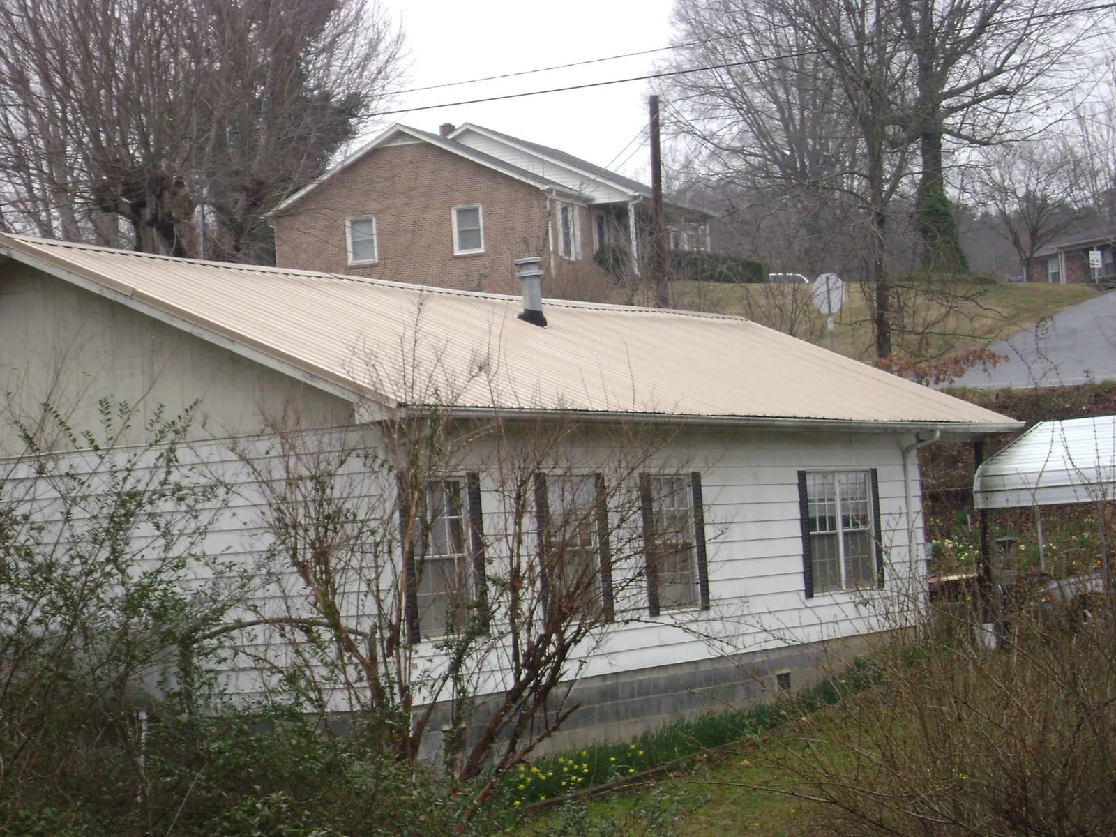 Tan metal roof on a white sided house set into a hillside — Commercial Roofing by Roofing Brothers in Lowry City