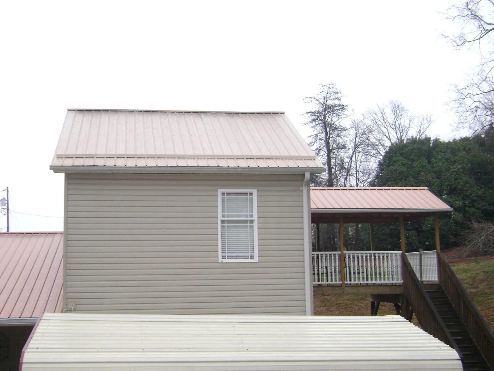 Tan metal roofs on a two story addition and attached porch, from a Roof Replacement job in Lowry City